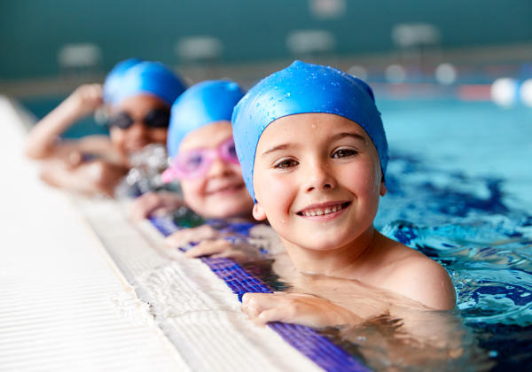 Portrait Of Children In Water At Edge Of Pool Waiting For Swimmi